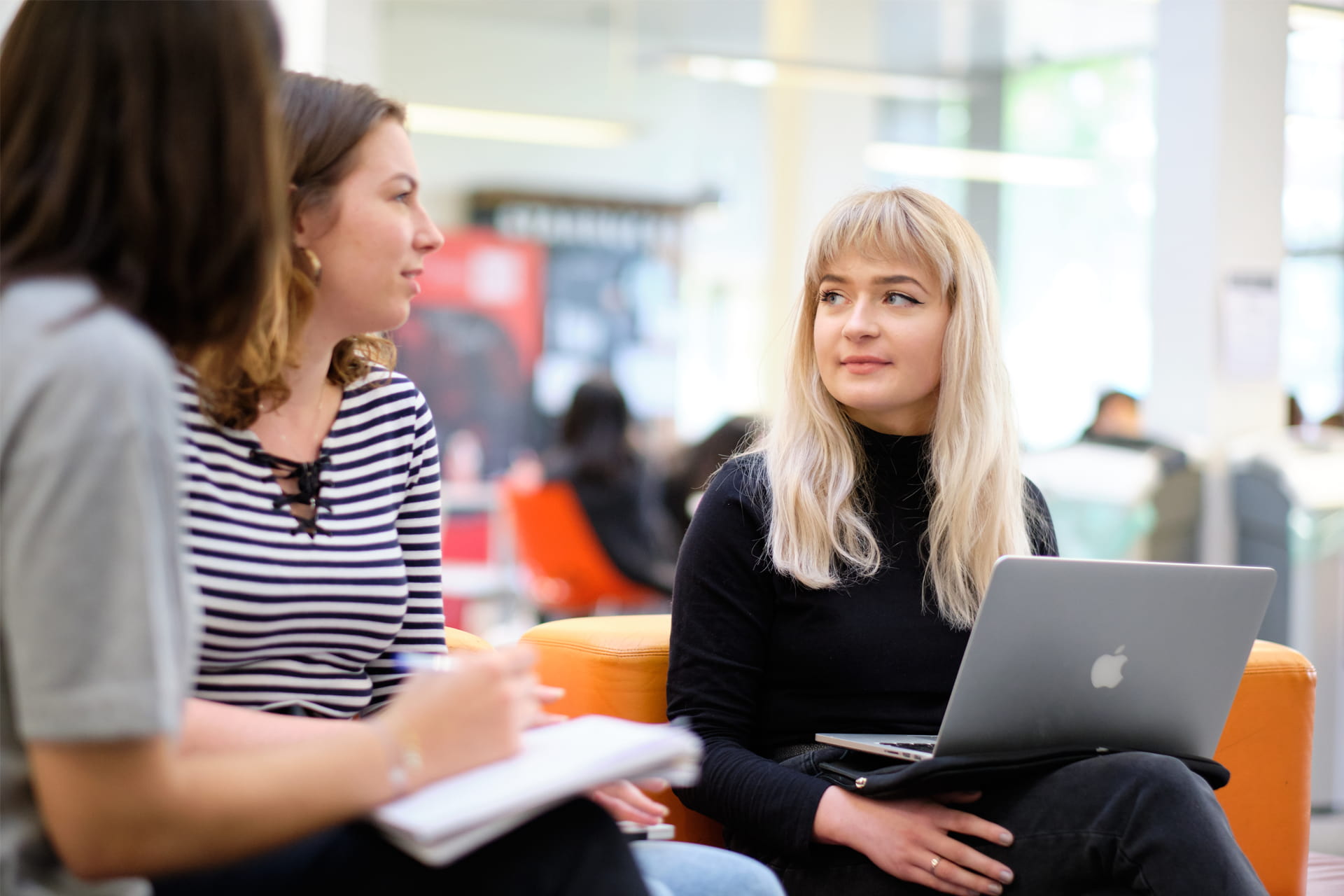 Three individuals sitting together in a bright indoor space, engaged in collaborative work.