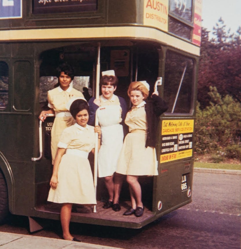 A colour photograph from the 1960s showing 4 nurses in their uniform on the open platform at the back of a green double decker bus.