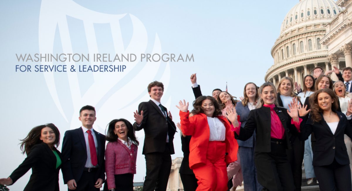A group of young women and men in business attire smiling and jumoing into the air. Behind them the US Capitol is visible.