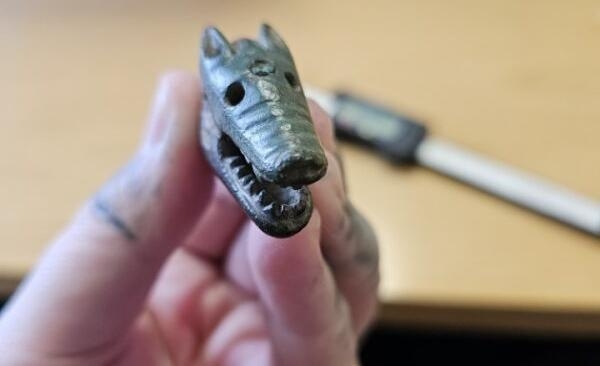 Viking dagger hilt in the shape of a wolf's head, held up carefully in one hand