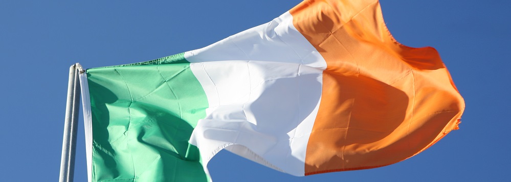 Irish tricolour flag on a pole against a blue sky 