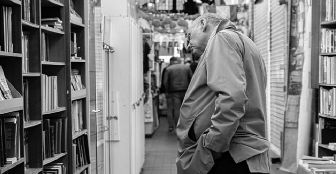 black and white photograph of a man peering sideways at bookshelves