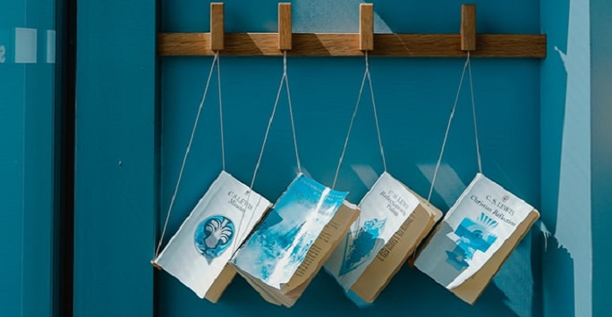 books hanging from their spines by string along a shelf
