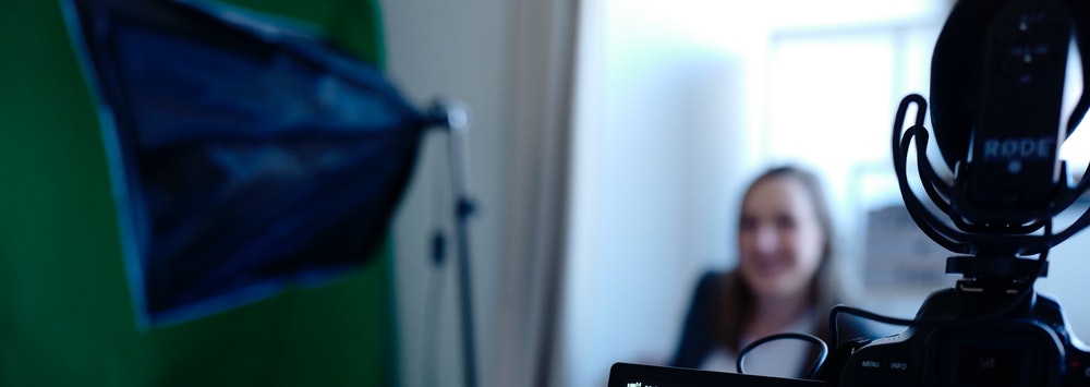 image of a woman being interviewed, slightly out of focus with a video camera screen in the foreground