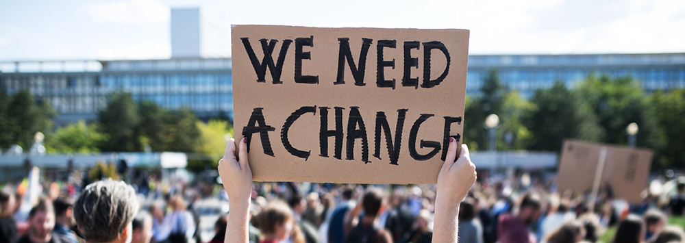 Image of protester with sign saying 'We Need A Change'