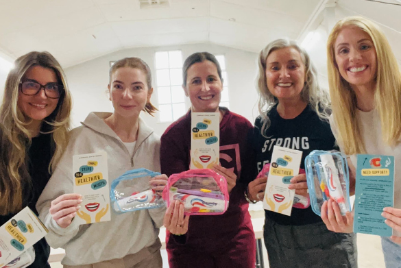 Five people standing indoors in a bright room holding oral health kits.