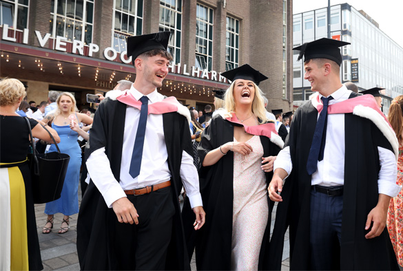 Students walking hand in hand wearing graduation cap and gowns