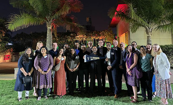 Staff and students group photo at University of Liverpool alumni event in India (colourfully-lit palm trees in the background against a nighttime backdrop)
