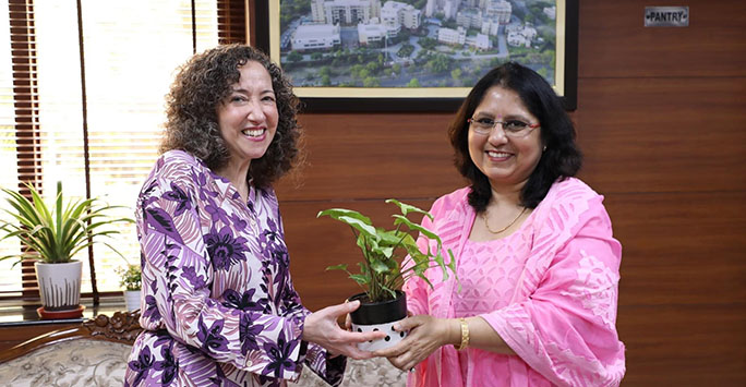 Prof Debra Morris at NLU Delhi, handing a plant to a female member of staff in a pink dress