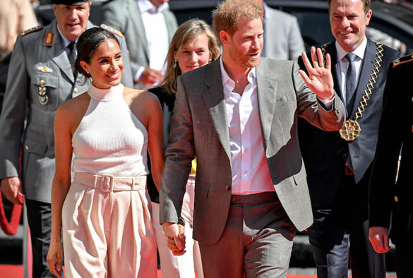 A photo of Prince Harry and Meghan Markle waving in a crowd.