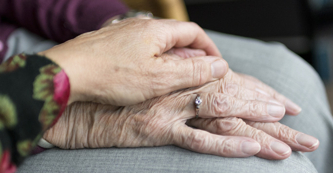 A hand resting on top of an eldery pair of hands.