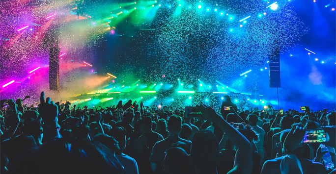 Crowded concert with a stage filled with coloured lights and confetti.