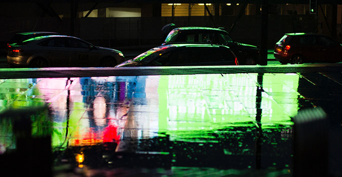 Image of street at night with parked cars and reflection from lights