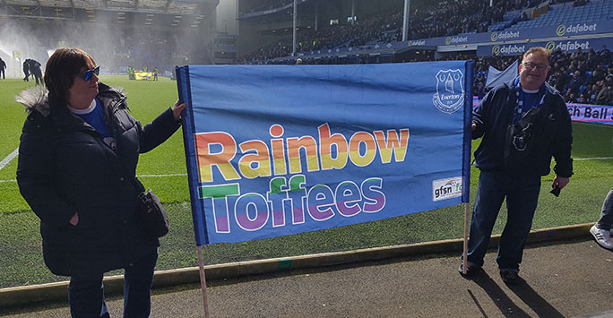Image of Dr Homfray with 'Rainbow Toffees' flag at Everton Football Club's home stadium, Goodison Park