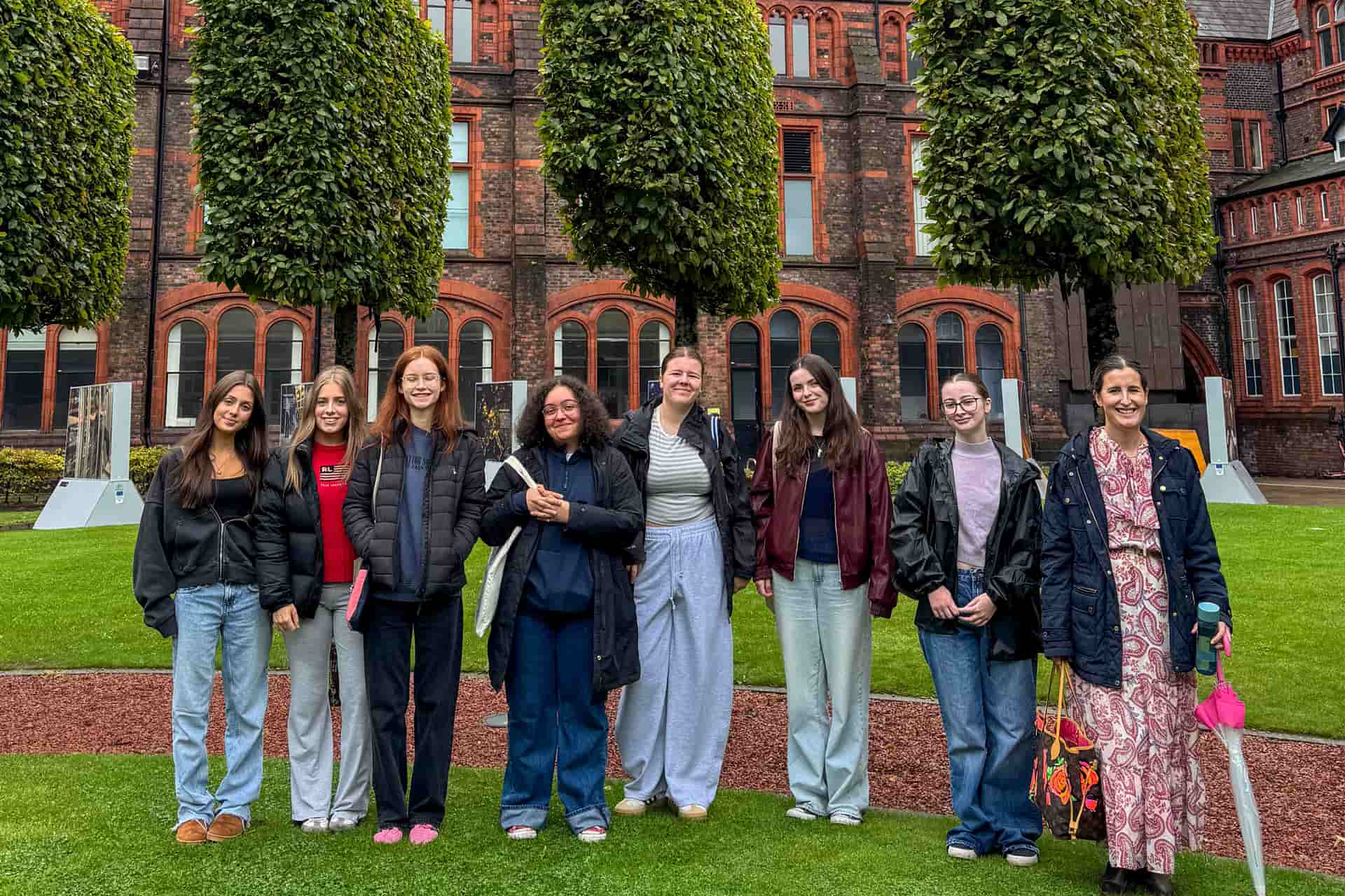 A group of students and a staff member standing together on the University of Liverpool campus during Welcome Week treasure hunt, smiling in front of the red-brick building.