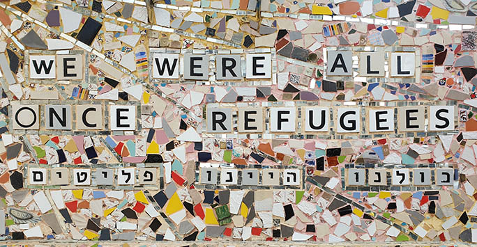 Tiled mosaic wall, colourful and patterned with the words 'we were all once refugees'