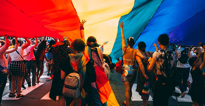 A group of people marching at pride under a rainbow flag