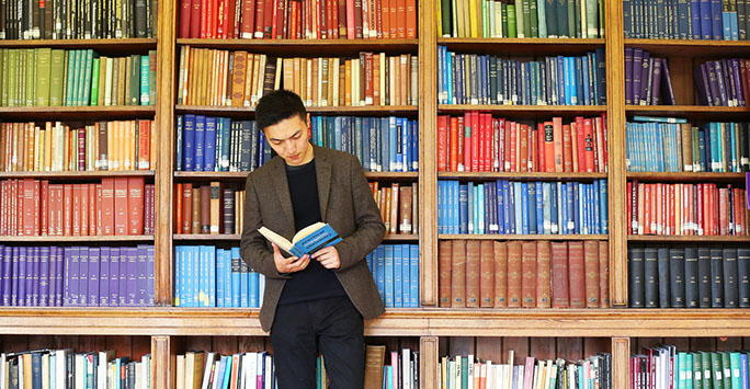 Picture of student reading book in front of large, colourful bookshelf