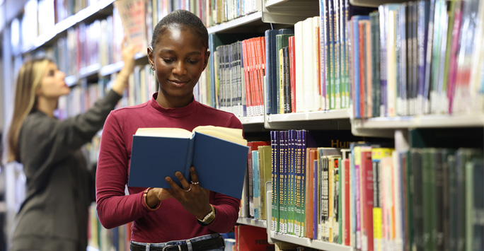 A student reading a book as she walks past a large bookshelf