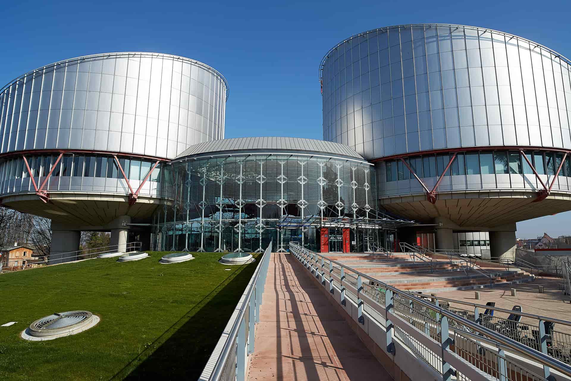 Modern architectural view of the European Court of Human Rights in Strasbourg, France, featuring twin cylindrical metal and glass towers connected by a central glass atrium.
