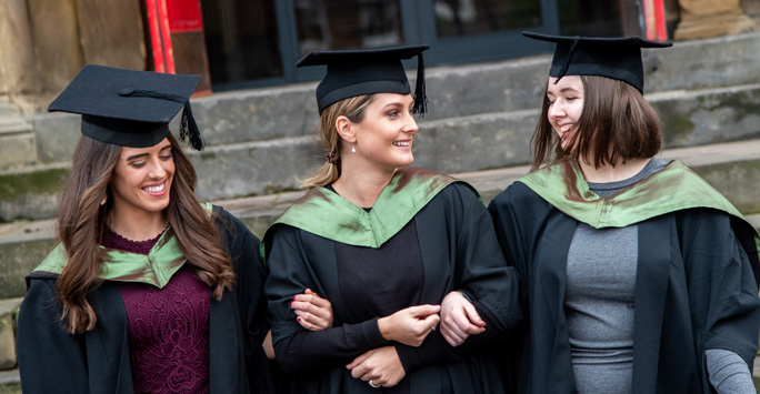 Three Law students arm in arm wearing their graduation cap and gowns.