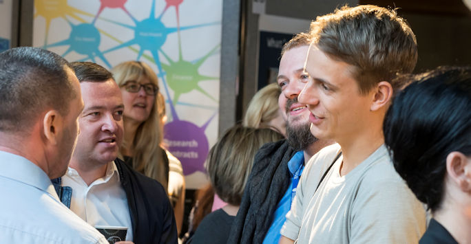 A group of people engaged in conversation, surrounded by others in a event setting.