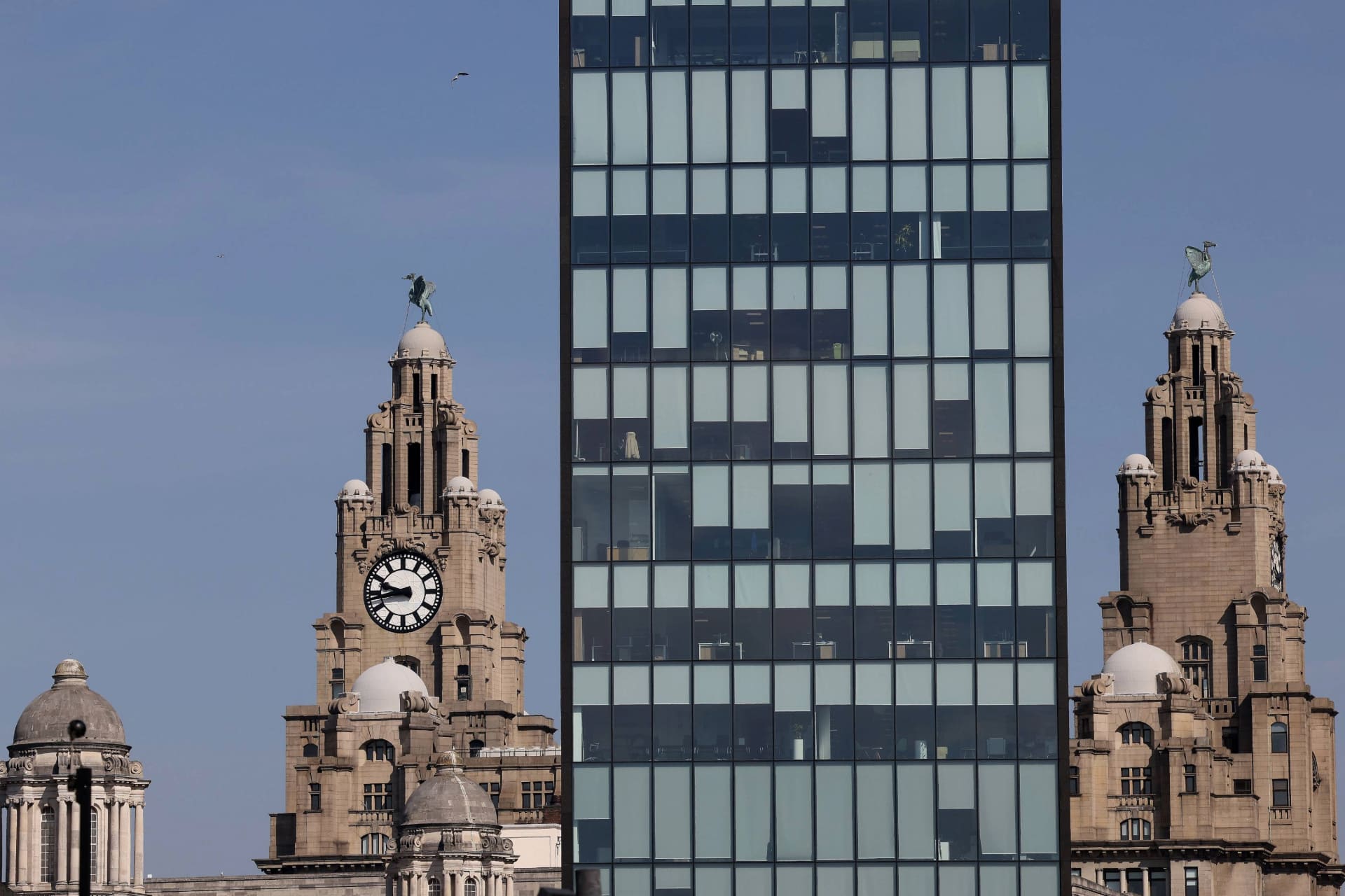 A modern glass building stands in front of the Liver Bird towers.
