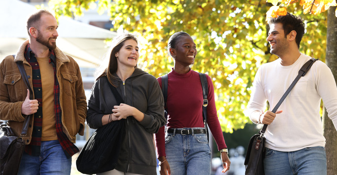 Four students walking through campus smiling