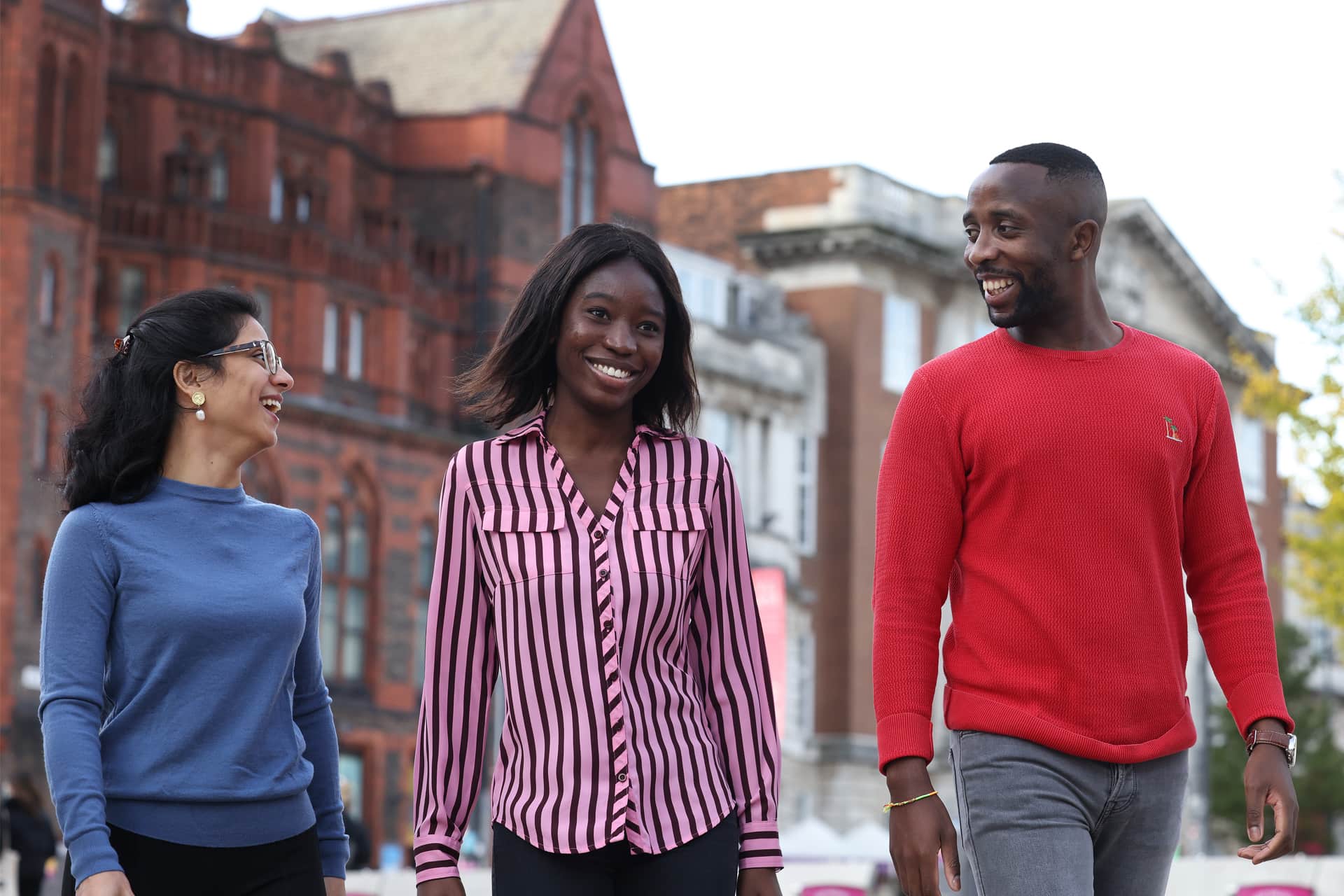 Three people walking together outdoors in front of historic red-brick university building.