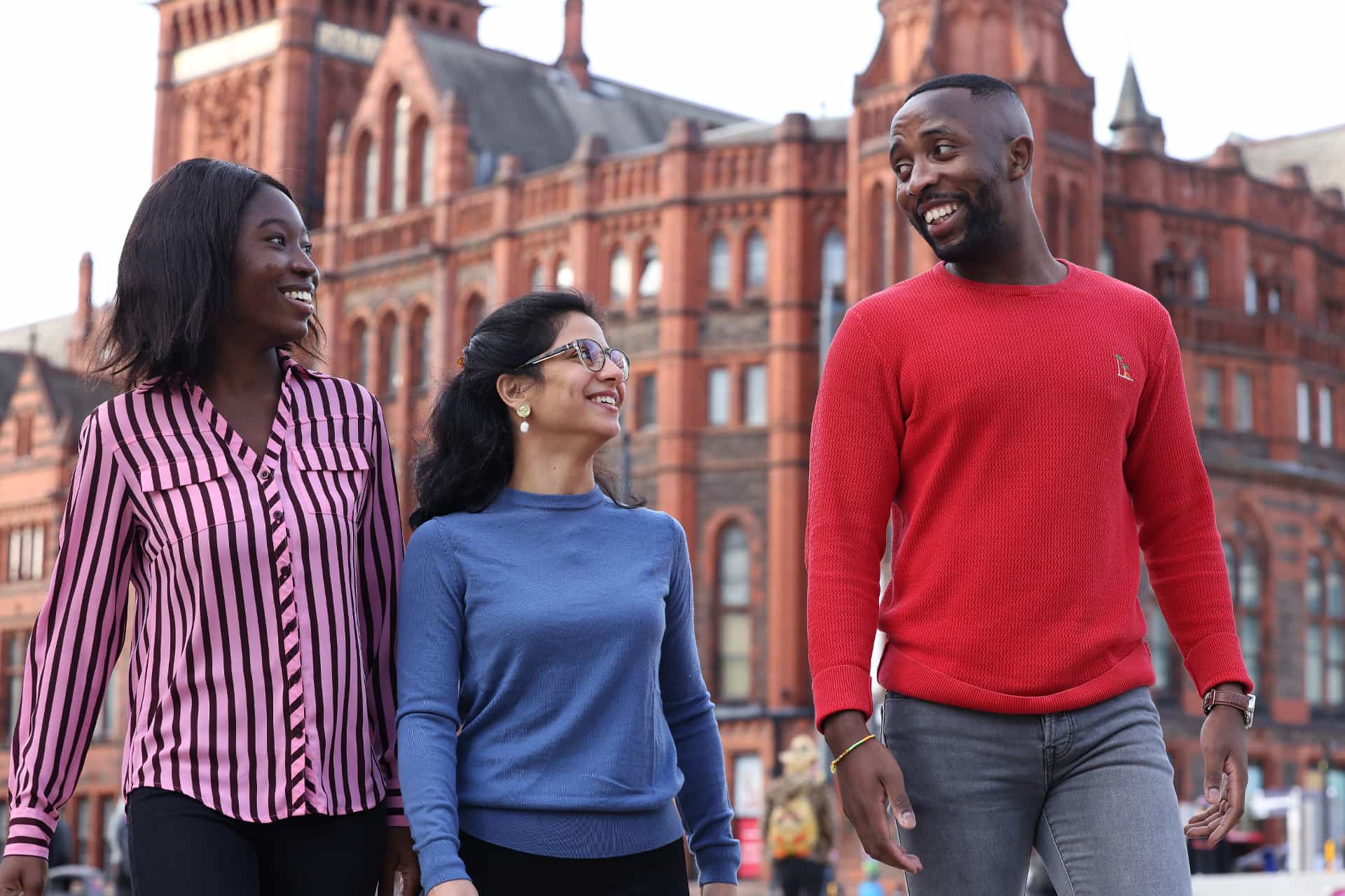 Three students walk together in front of the historic red brick building.