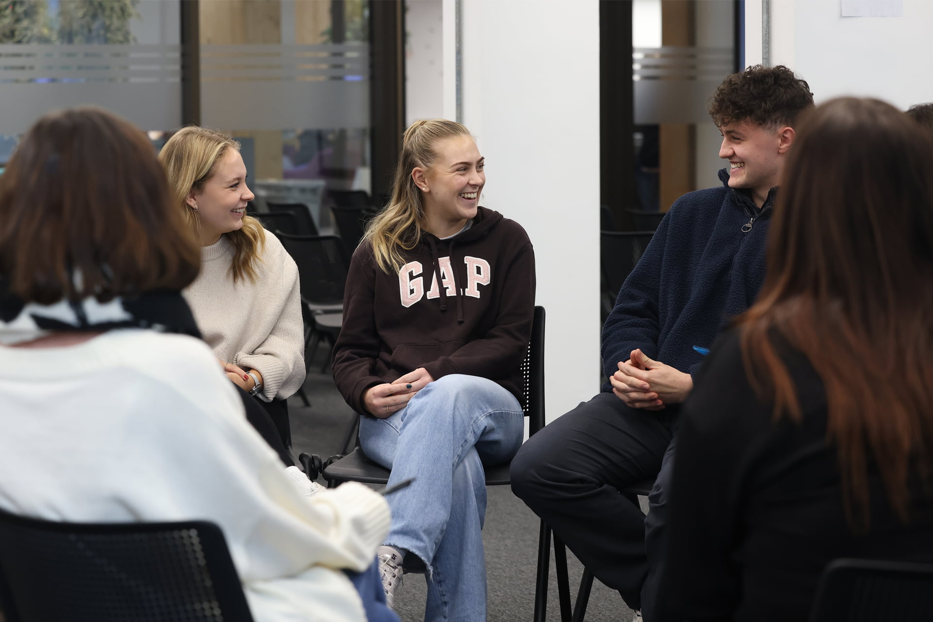 A group of people sitting in a circle on chairs, engaged in conversation.