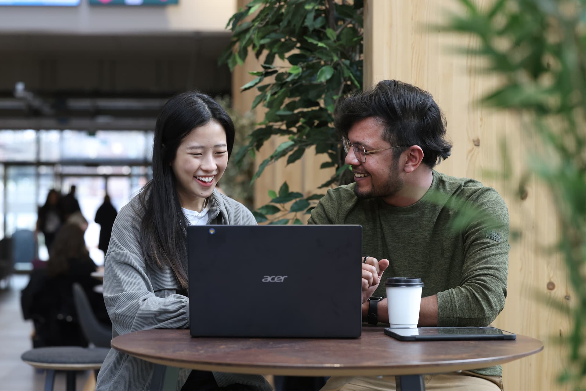 Two people sitting at a small table in a modern indoor space, working together on a laptop.