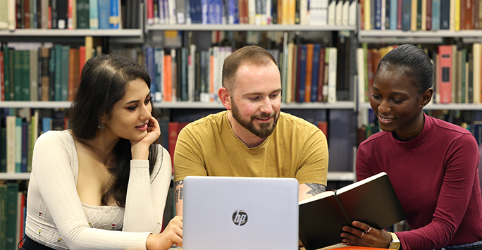 A picture of three students looking over a laptop