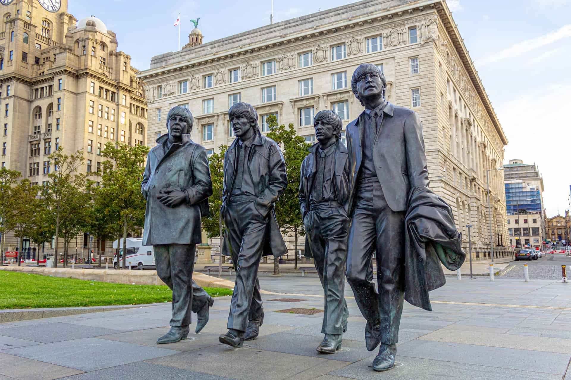 Bronze statues of the Beatles walking together, placed in front of historic buildings along Liverpool’s waterfront.