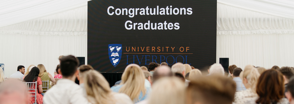 A room of people sat facing a television that reads 'Congratulations Graduates'