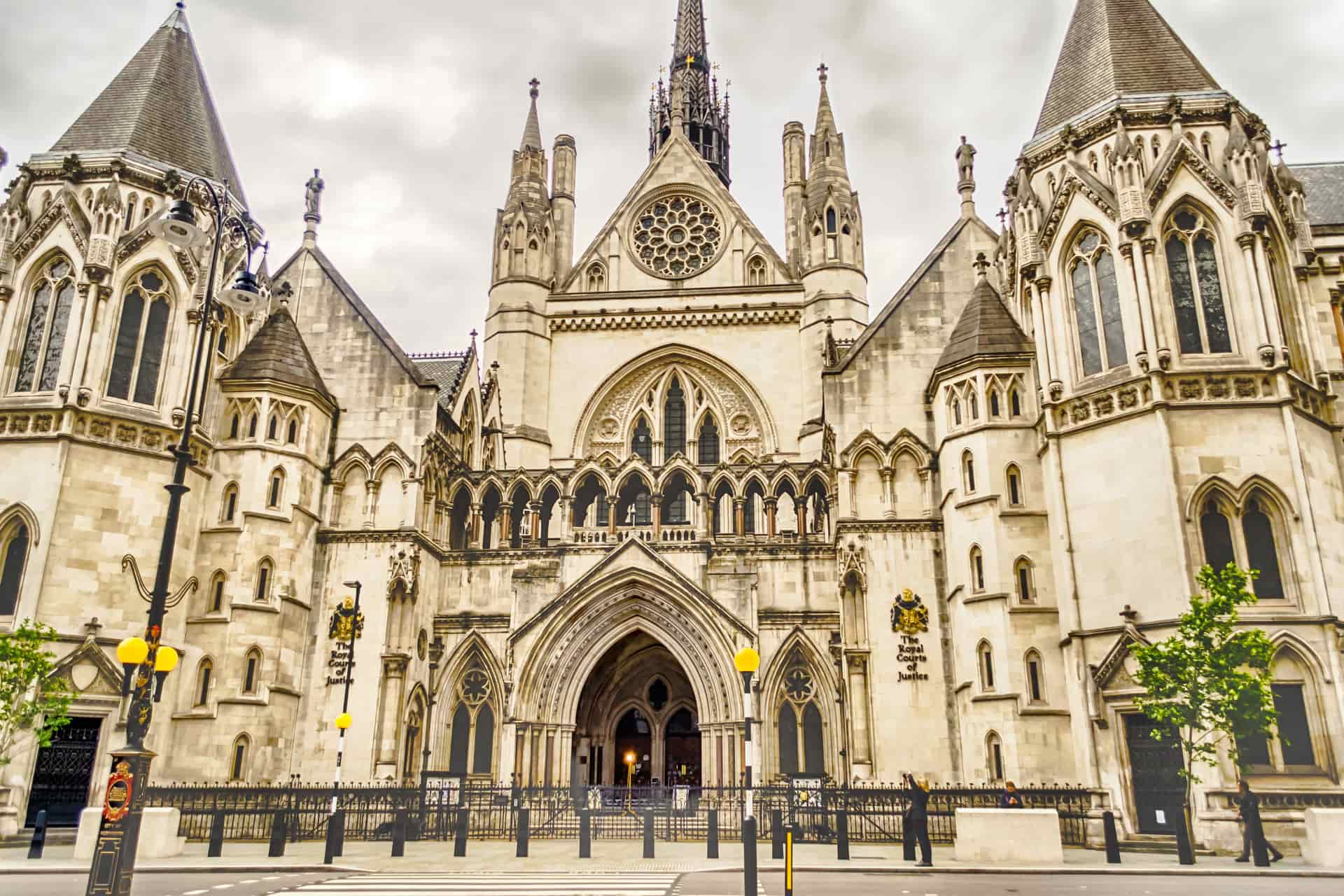 The facade of the Royal Courts of Justice in London, featuring Gothic architecture with pointed arches, intricate stone carvings, tall spires, a central rose window, and two symmetrical towers.