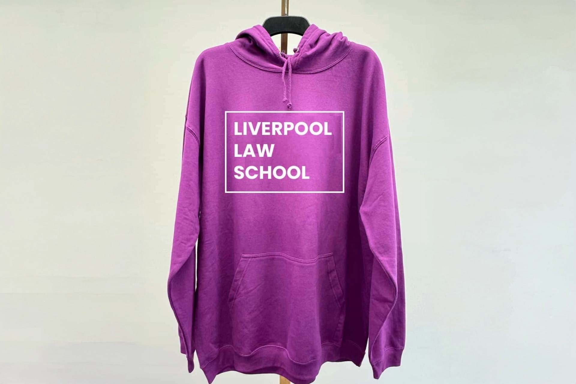 Purple hooded sweatshirt with a front pocket, featuring white text inside a rectangular box that reads ‘LIVERPOOL LAW SCHOOL'.