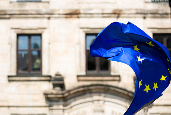 A photograph of the European flag flying in the wind infront of an old building