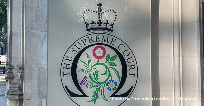 Photograph of The Supreme Court crest on a sign outside the Supreme Court. (Photo by Francais a Londres for Unsplash)