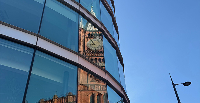 Victoria clock tower reflected in the glass curve of the Foundation Building