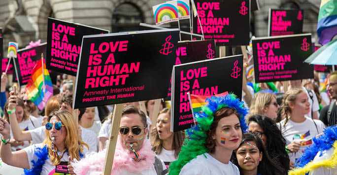 A collection of people walking through the street holding signs that read 'Love is a human right'.
