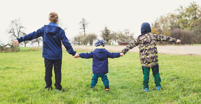 Three children holding hands at a park