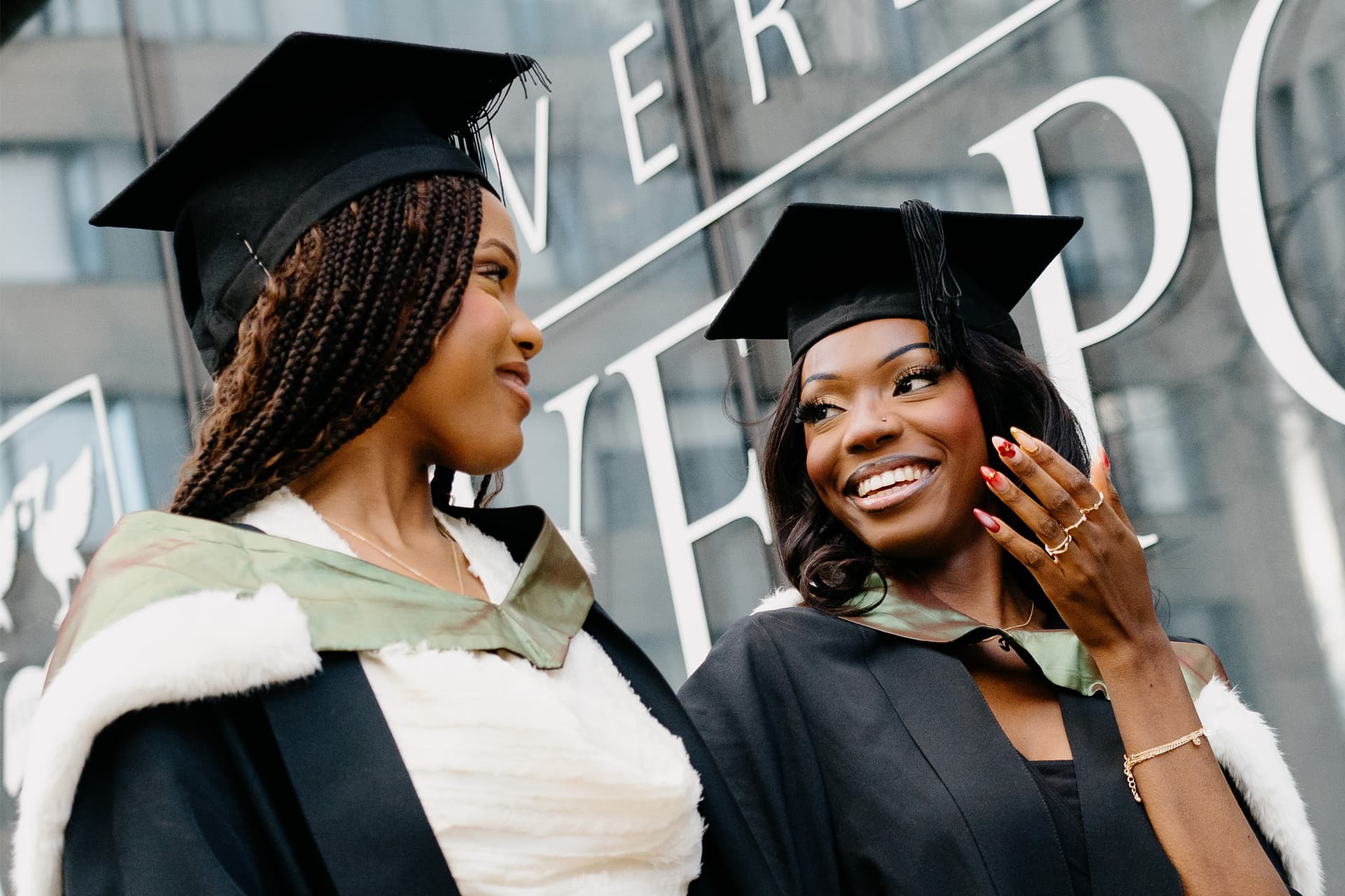 Two students dressed in graduation cap and gowns walk together smiling.