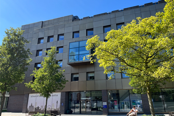The exterior of the School of Law and Social Justice - a modern building featuring a bronze facade surrounded by lush green trees.
