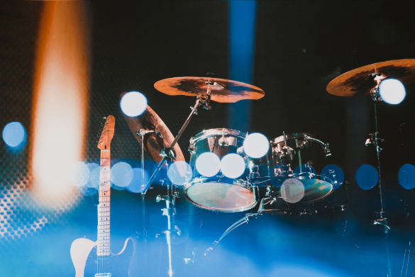 Stage setup featuring a drum kit and an electric guitar, illuminated by colourful concert lighting.