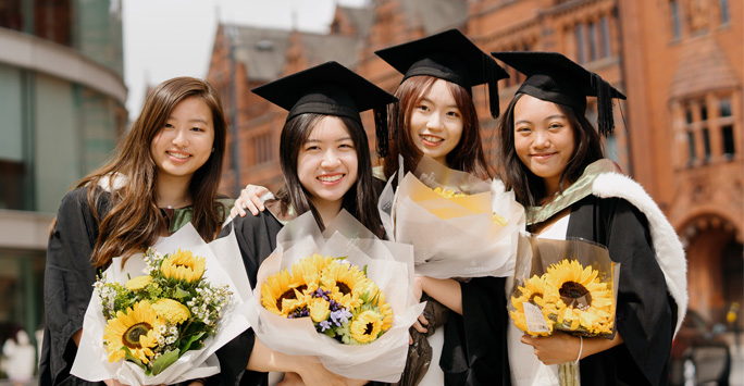 Students in graduation robes each holding a bunch of flowers.