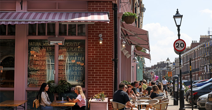 People sat on tables outside a cafe on a sunny day.