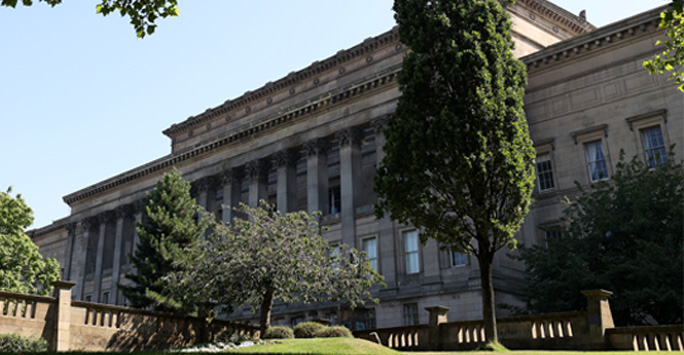 St George's Hall. A grand looking Neoclassical building surrounded by trees.