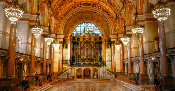 The Great Hall, a large room with barrel-vaulted ceiling. The hall is adorned with statues of notable figures and illuminated by pretty chandeliers.