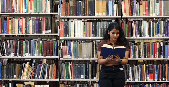 A student reading a book against a large shelf of books